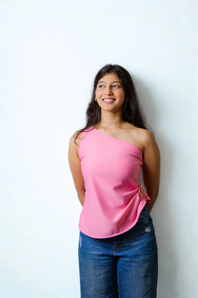 A model in a pink one-shoulder top against a pale wall