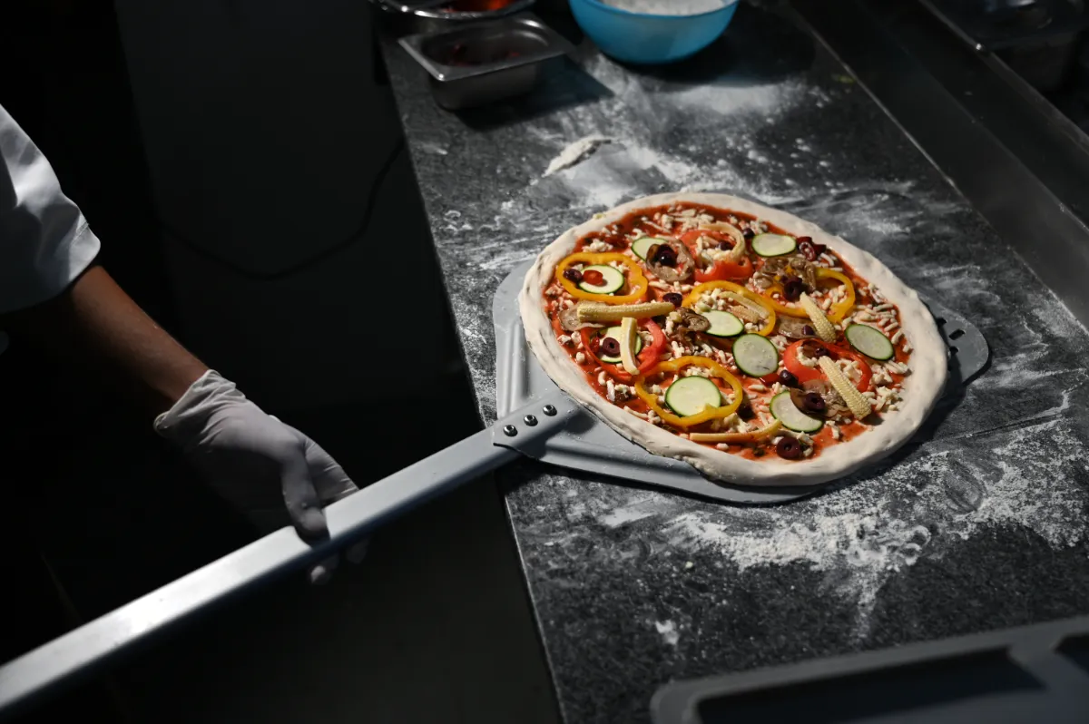 A dressed pizza going into the oven on a peel